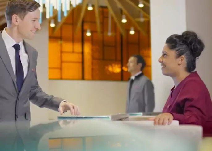 Business professional speaking with a receptionist in a hotel-style lobby, representing content marketing for travel audiences.